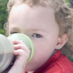 Young boy using sippy cup to drink beverage outdoors