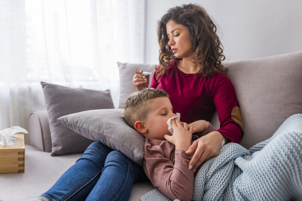 Young mother, holding her little sick boy fighting a winter virus, lying together on the couch