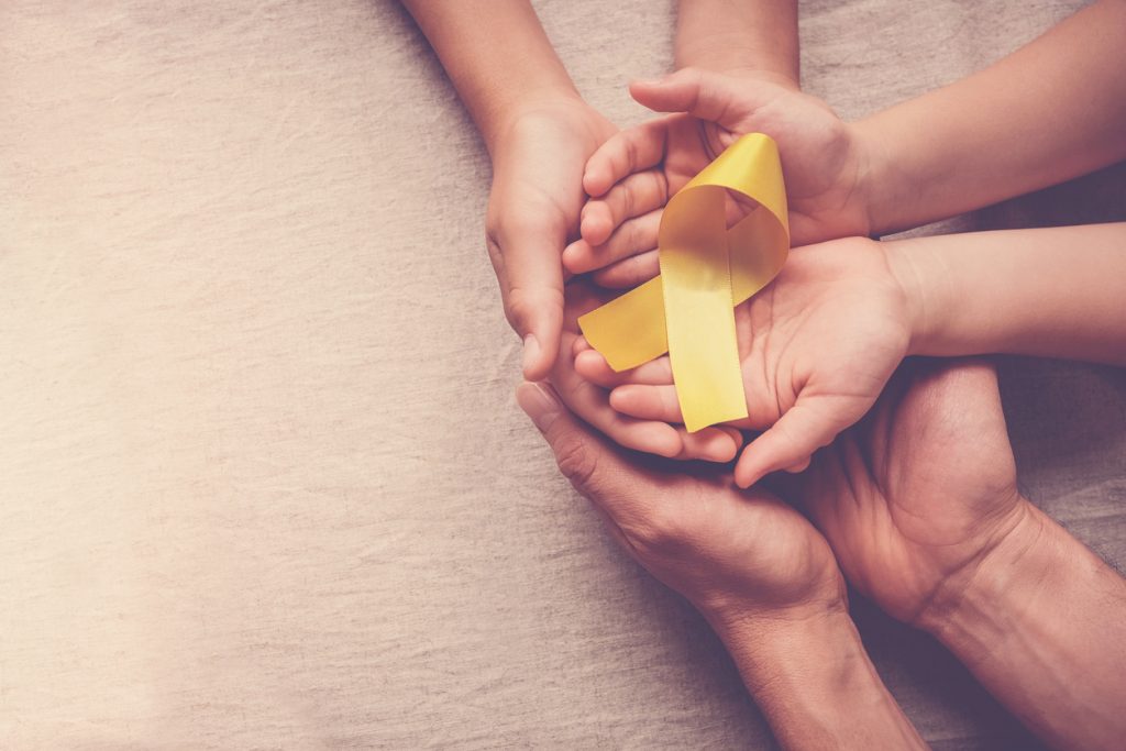 parents and child hands hold a yellow ribbon signifying childhood cancer awareness
